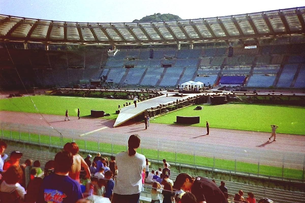 Fans watching from the lower stand as crew work on a stage built across the Stadio Olimpico pitch