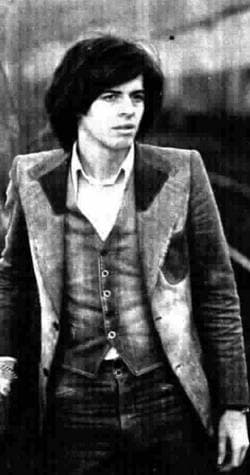 Claudio Baglioni standing in a three-piece suit with long dark hair, black and white