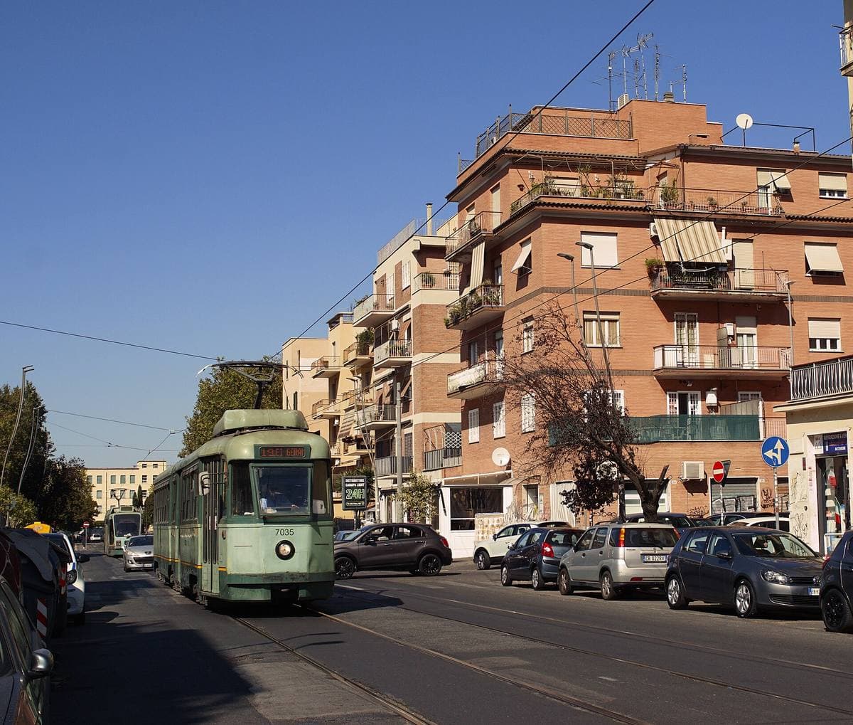 A green Rome tram passing apartment blocks with balconies on a sunny street