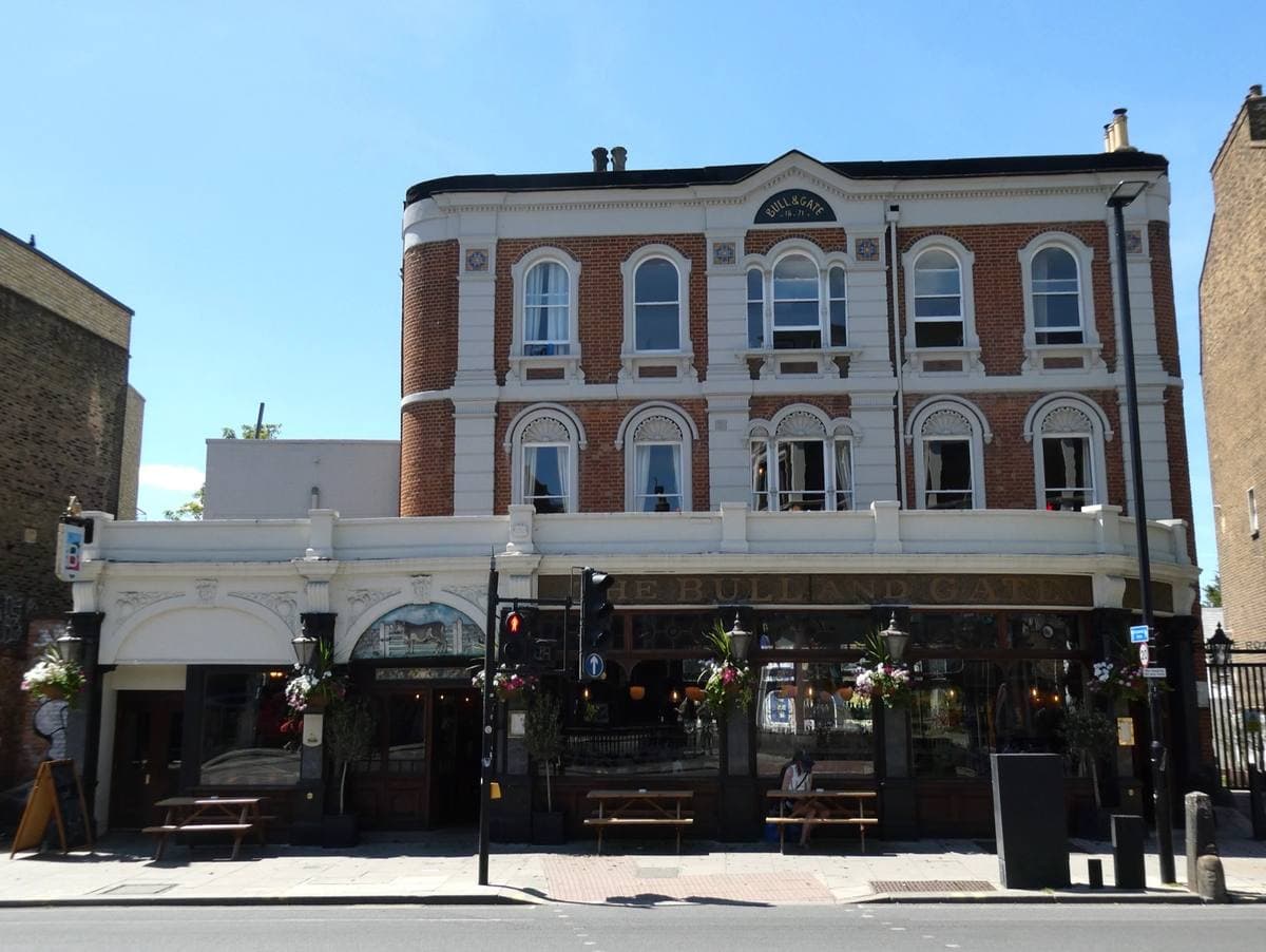 A tall Victorian pub with arched windows and benches outside on a sunny evening