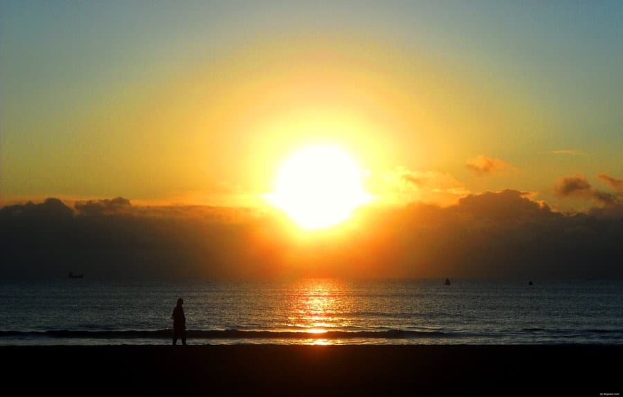 The sun rising over the sea, a lone figure on the wet sand in silhouette