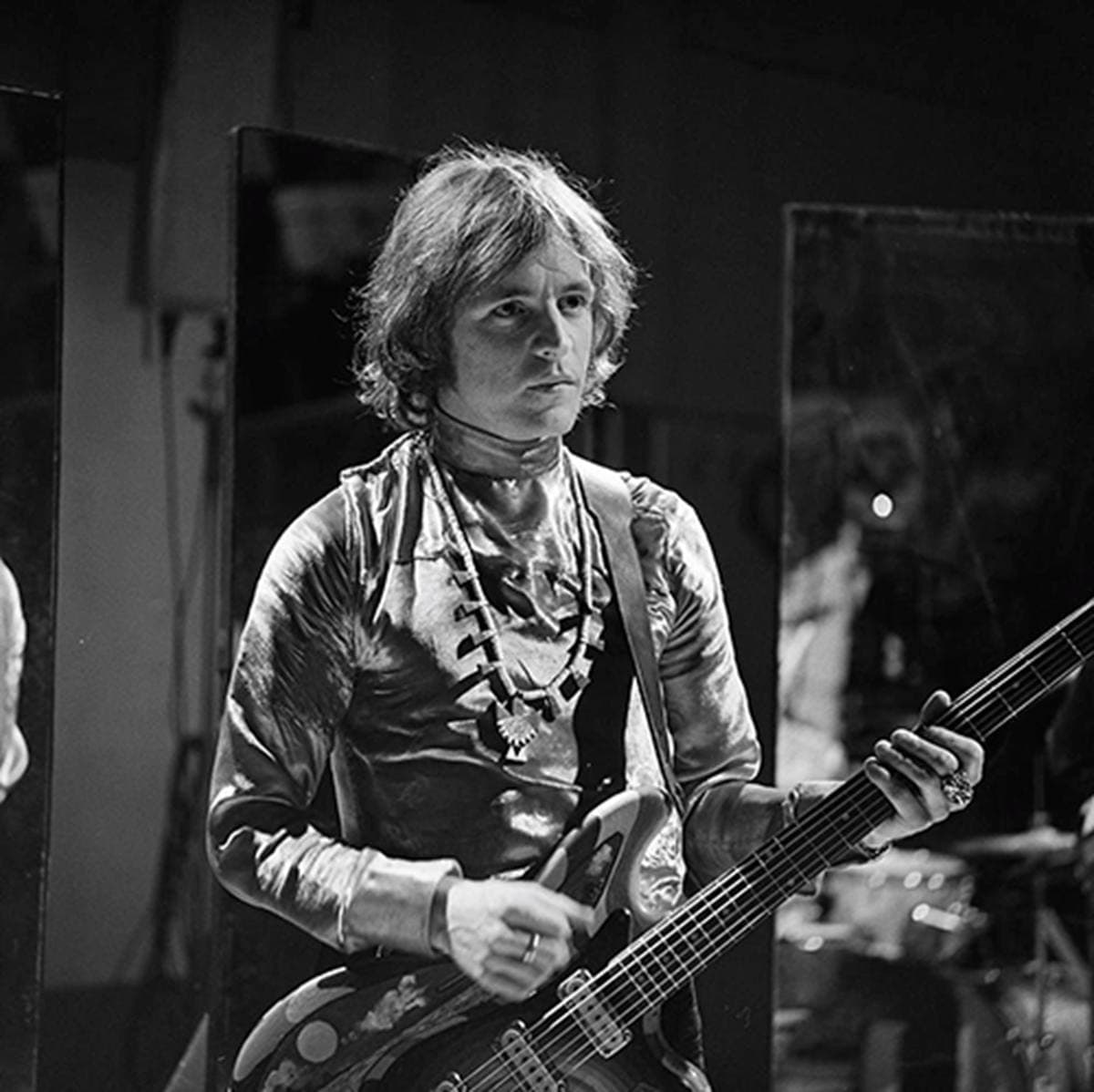 Jack Bruce singing into a microphone, playing bass, in a television studio, black and white