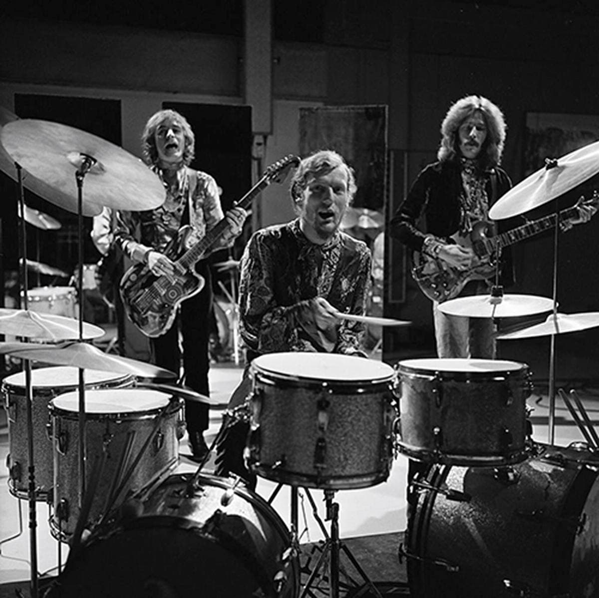 Cream playing in a television studio, a large drum kit in the foreground and Eric Clapton with a guitar at the back right