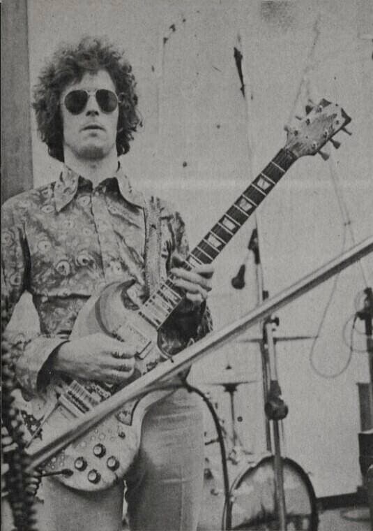 Eric Clapton in sunglasses and a patterned shirt playing a painted guitar