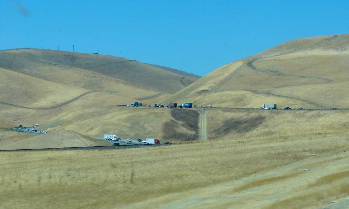Dry golden hills with wind turbines either side of a highway