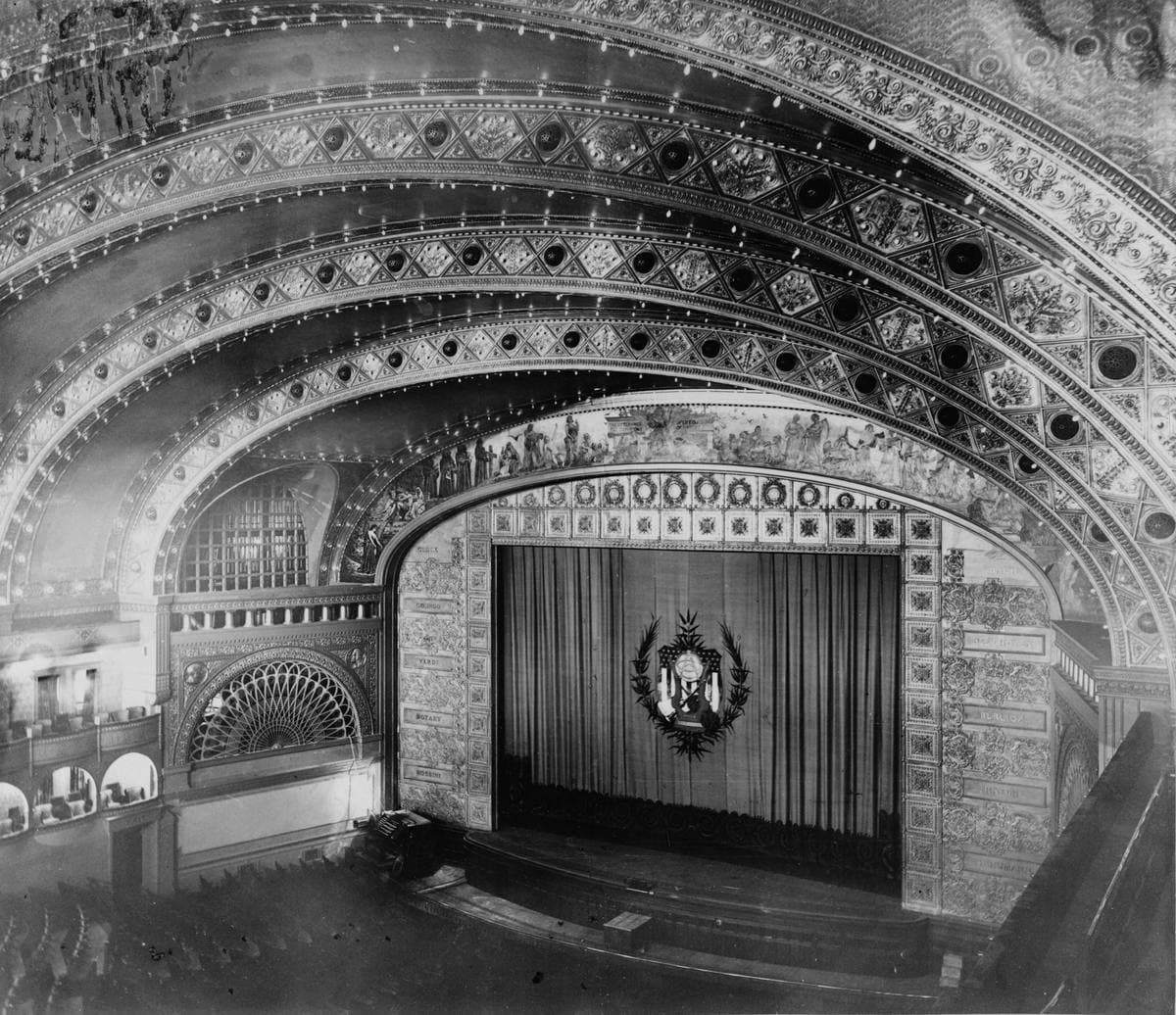 An old photograph of a vast theatre with arched gilded ceiling bands and tiers of seats