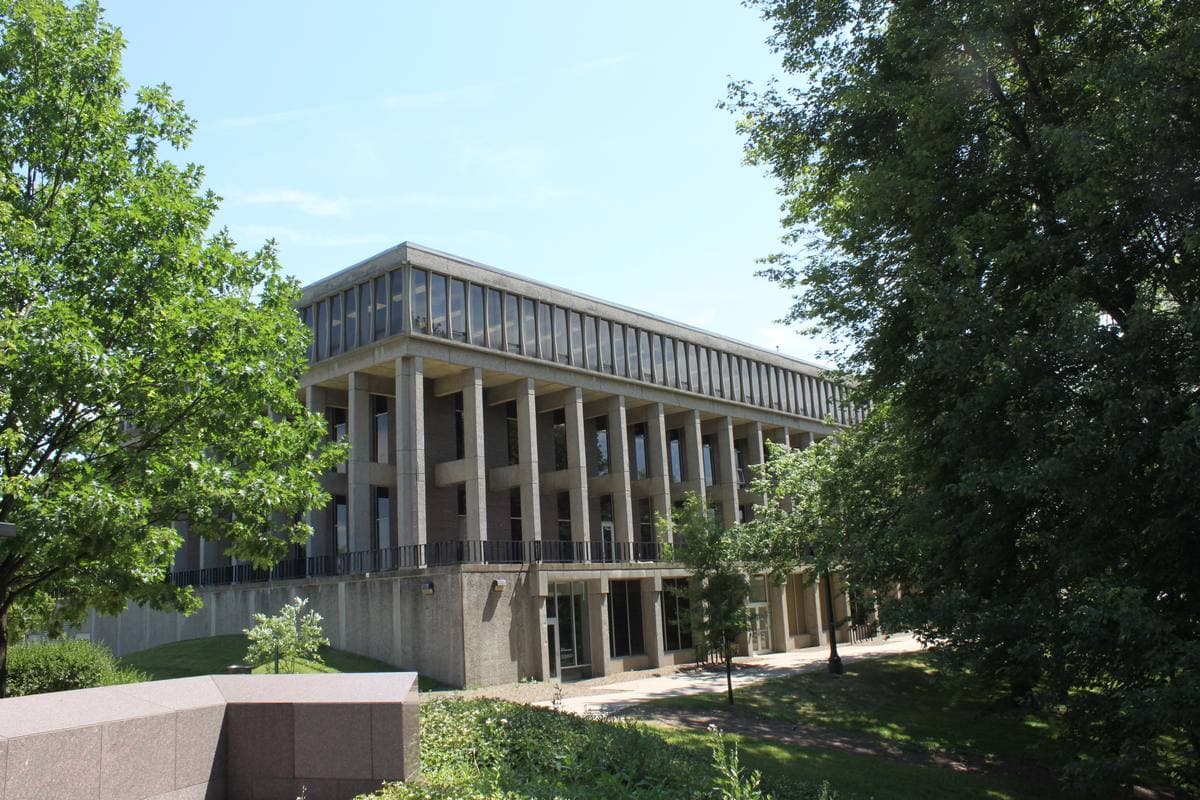 A modern building with tall square columns behind green trees