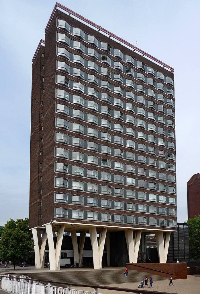 A tall concrete tower block standing on stilts over a town square