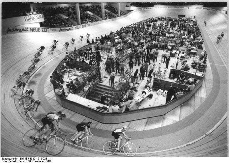 A black and white view of a banked cycle track inside a large indoor hall