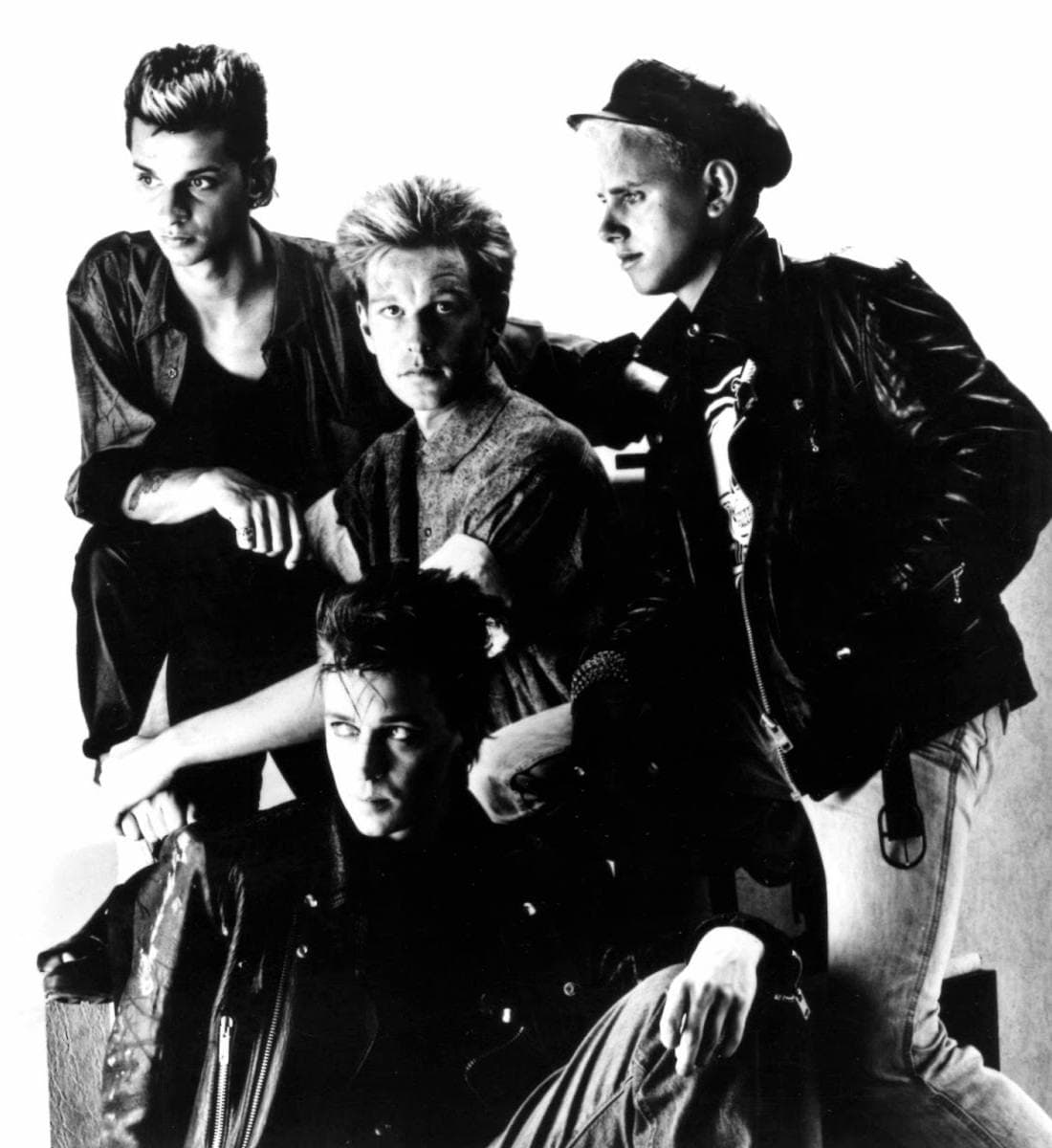 Four men in black posed close together in a publicity photograph