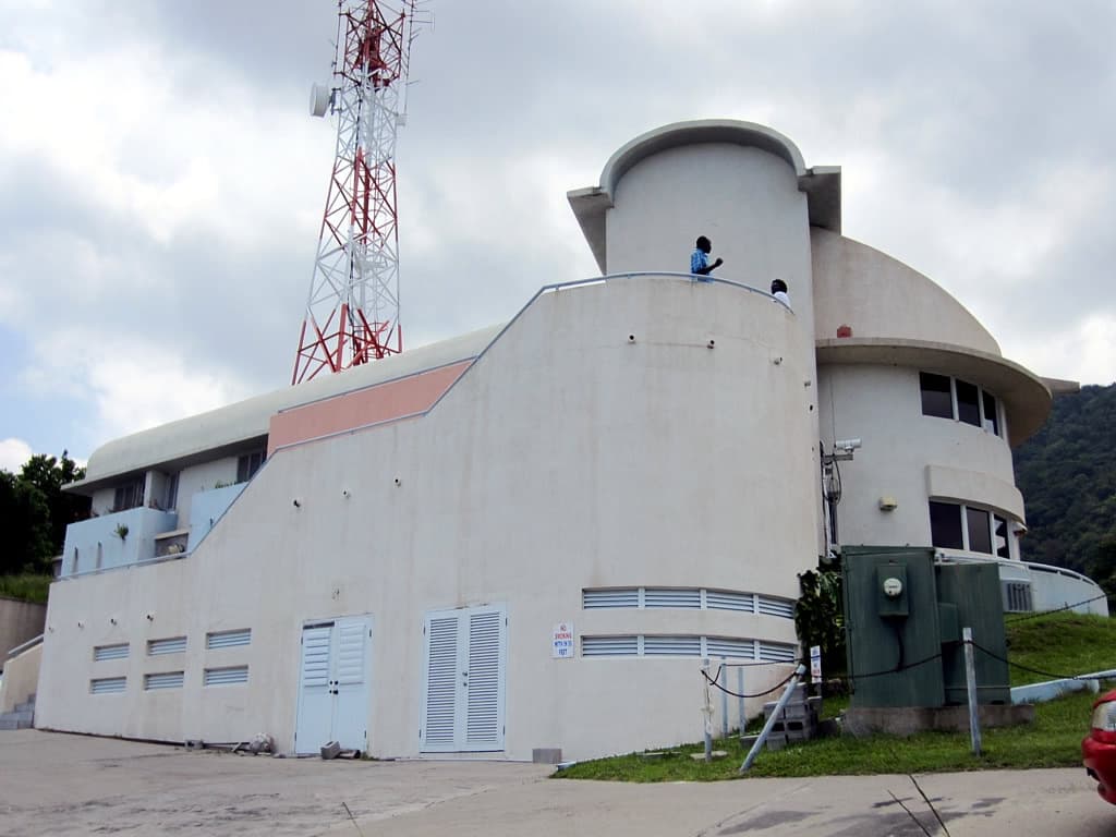 A white curved building with a radio mast and a viewing deck on a hillside