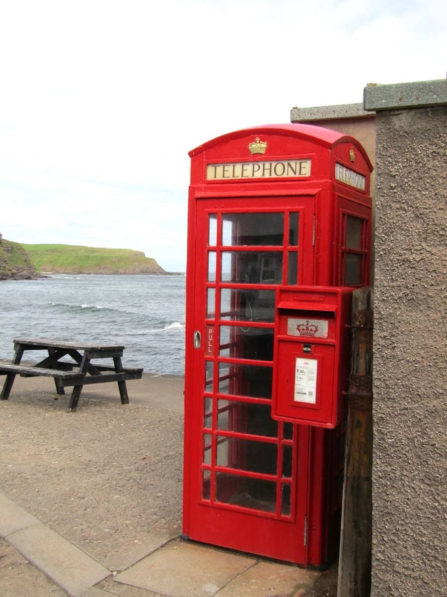 A red telephone box beside a harbour wall with the sea behind