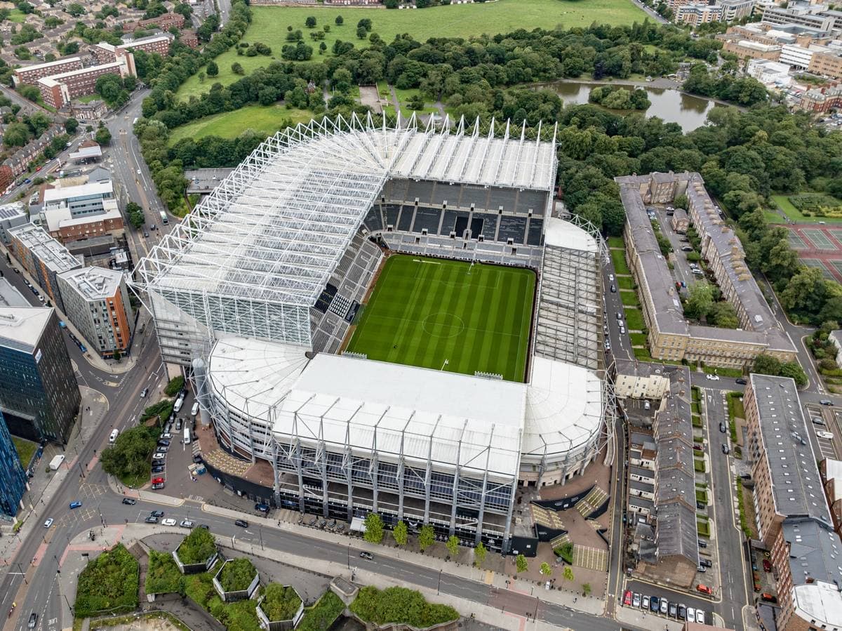 Aerial view of St James’ Park football stadium with its white roof, green pitch and the city around it