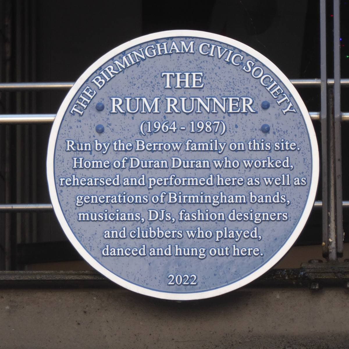 A round blue plaque for the Rum Runner club on a brick wall