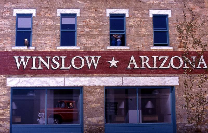 A painted two-storey shopfront wall with windows that reflect a street and a red pickup truck