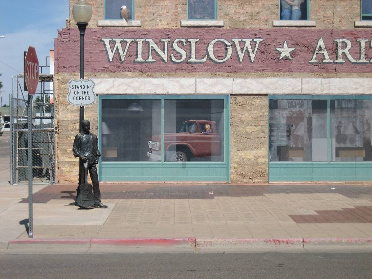 A bronze statue of a man with a guitar on a street corner in front of a painted brick wall