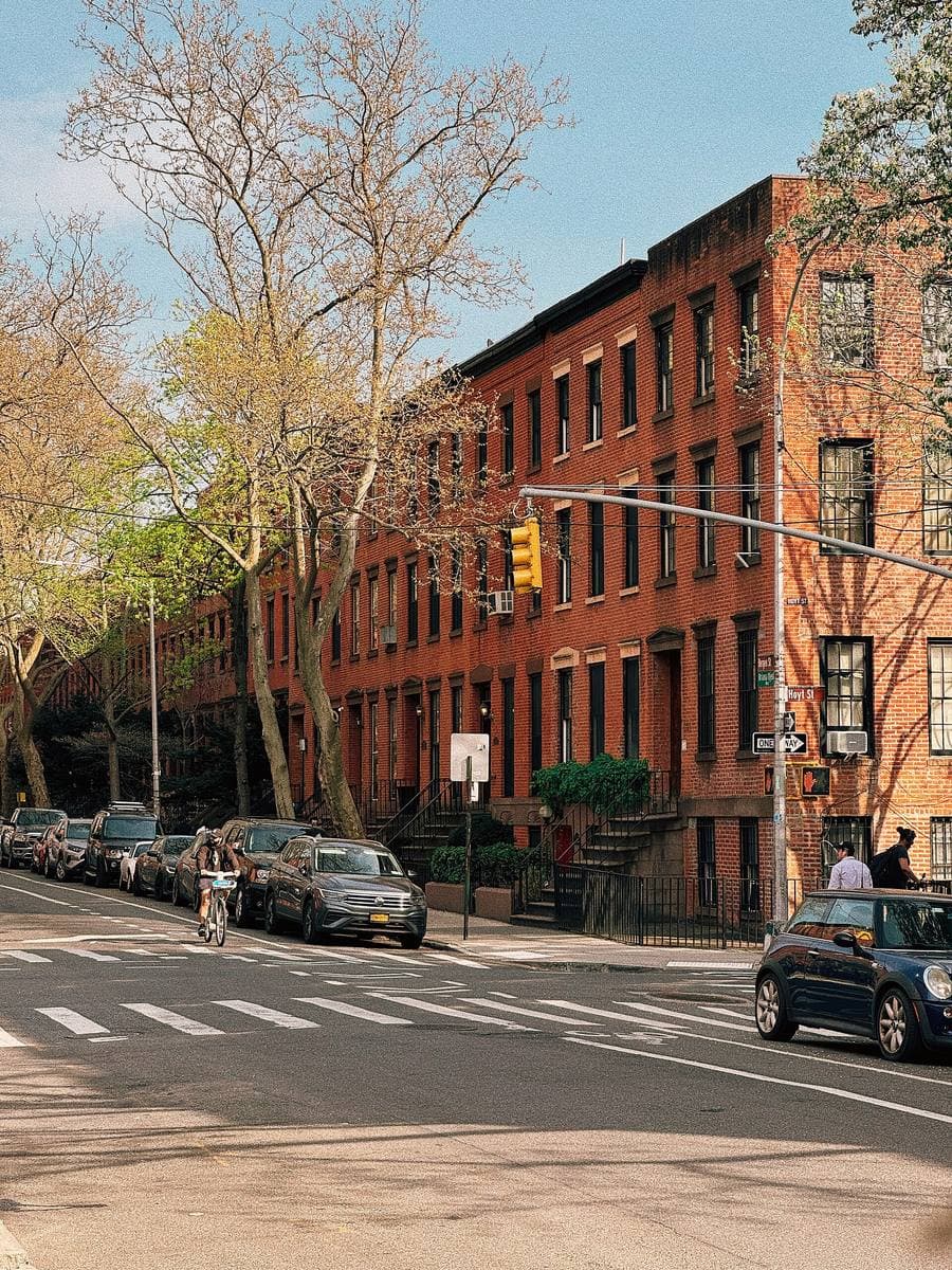 Red-brick rowhouses along a Brooklyn street in spring, a crossing in front