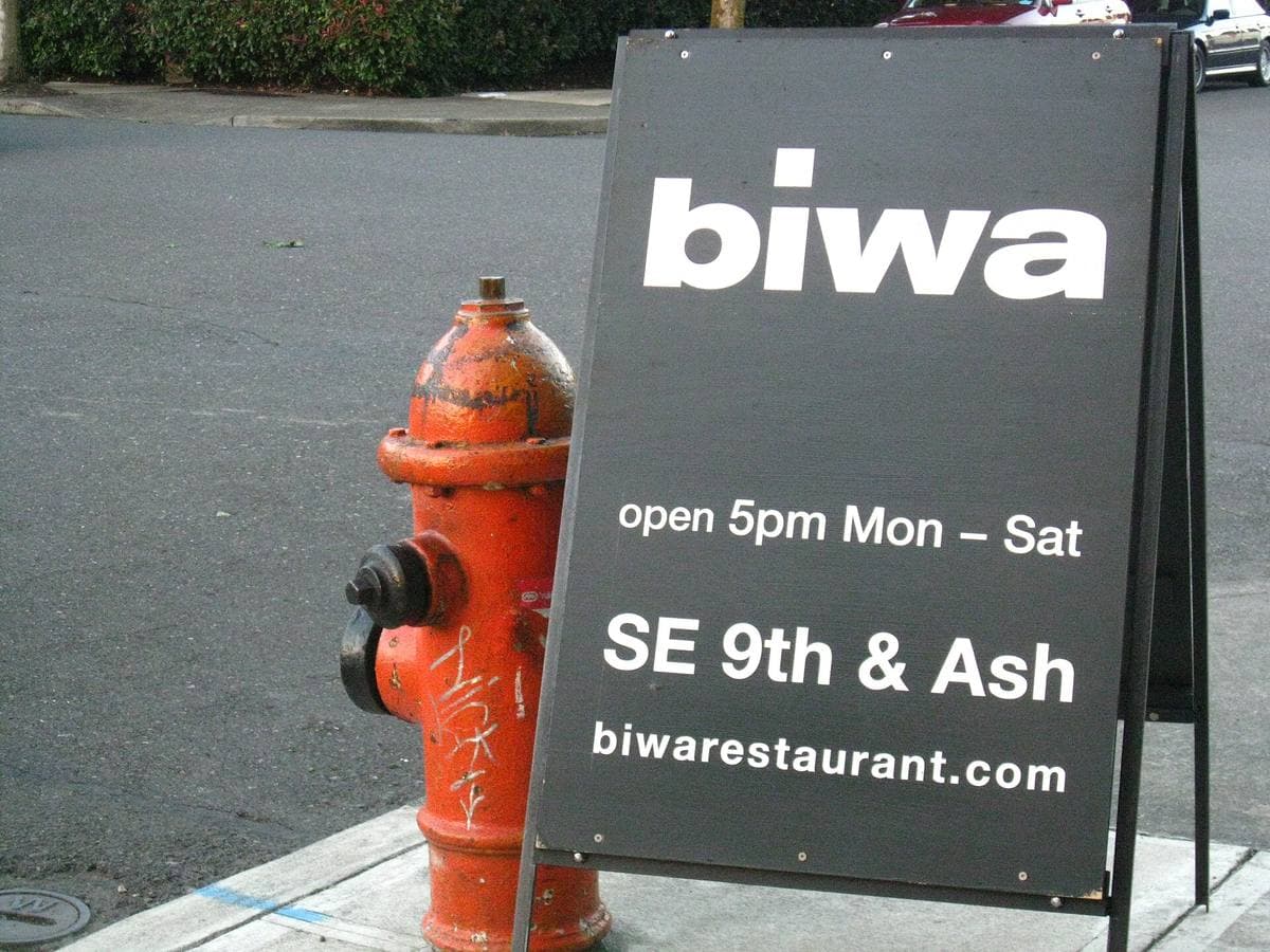A black pavement sign for a restaurant beside a red fire hydrant on a Portland street corner