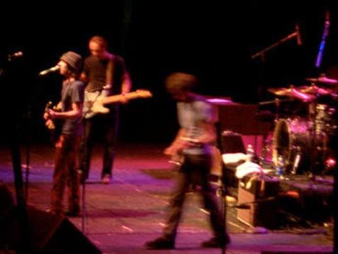 A band on a dark stage under purple light, a singer in a knitted cap at the microphone on the left
