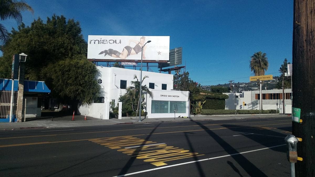 A wide boulevard in Los Angeles under a blue sky, a white building and a billboard ahead