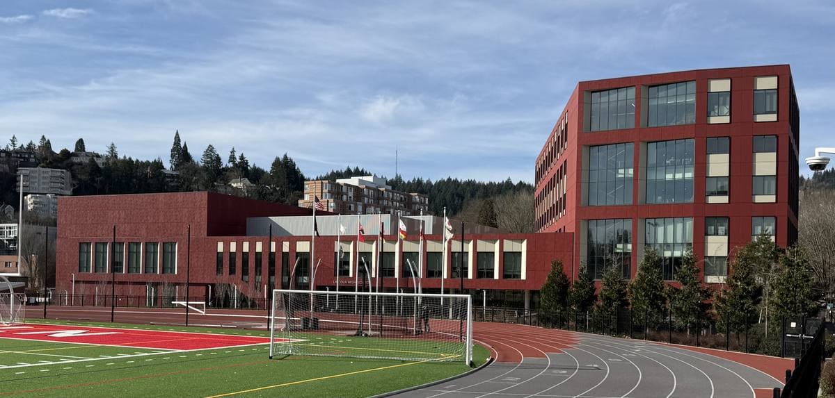A red-brick school building beside a running track and football pitch