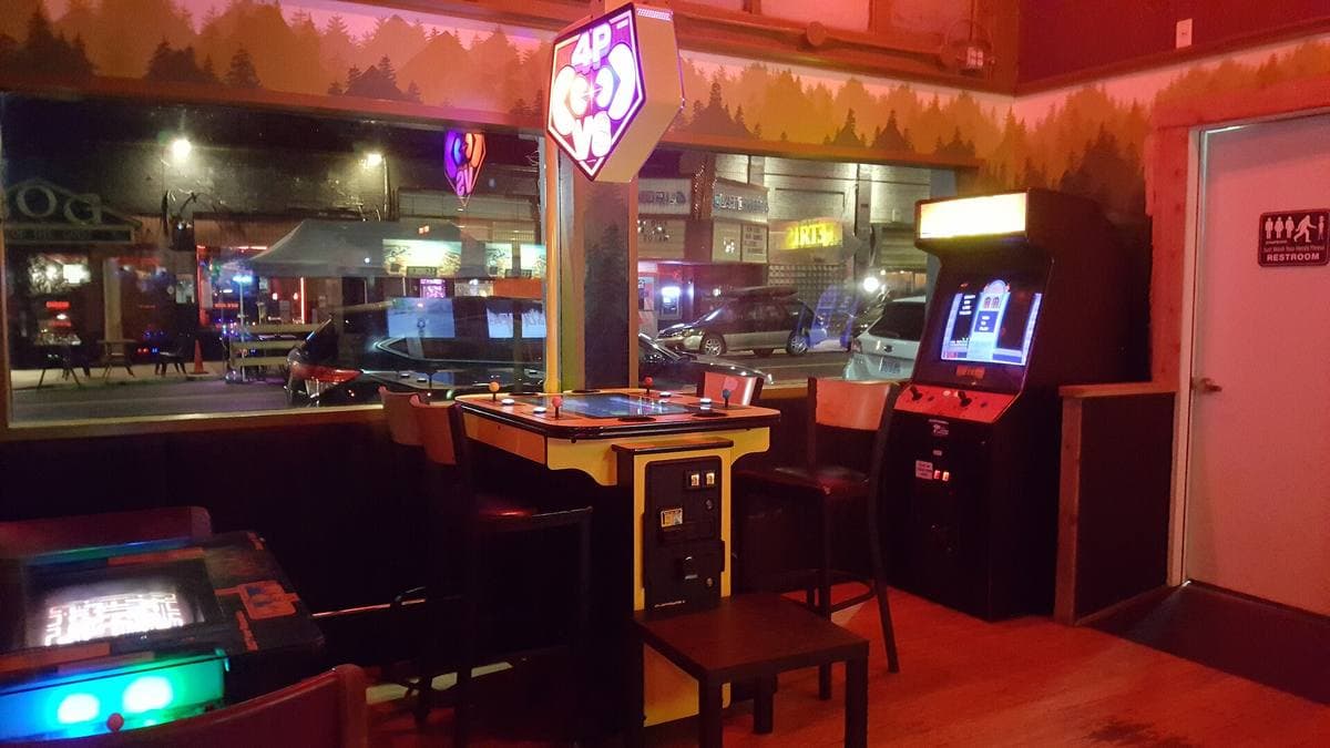 A dim bar lit red and violet, with arcade machines along the wall