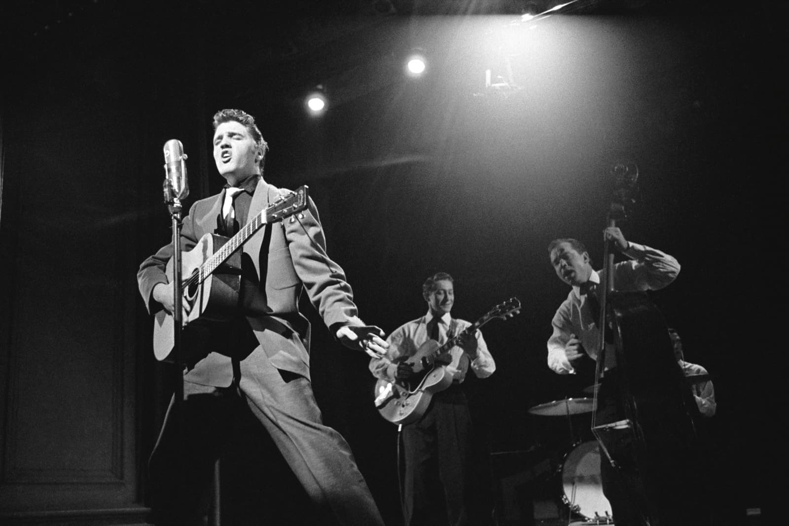 Elvis singing on stage with a guitarist and a double-bass player