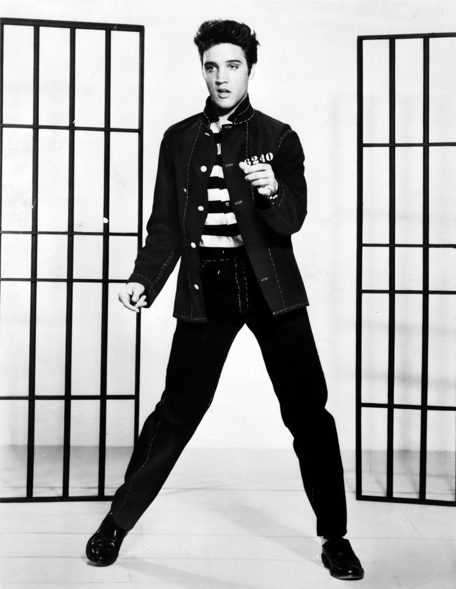 Elvis in a dark denim jacket and striped shirt, mid-dance between two sets of bars