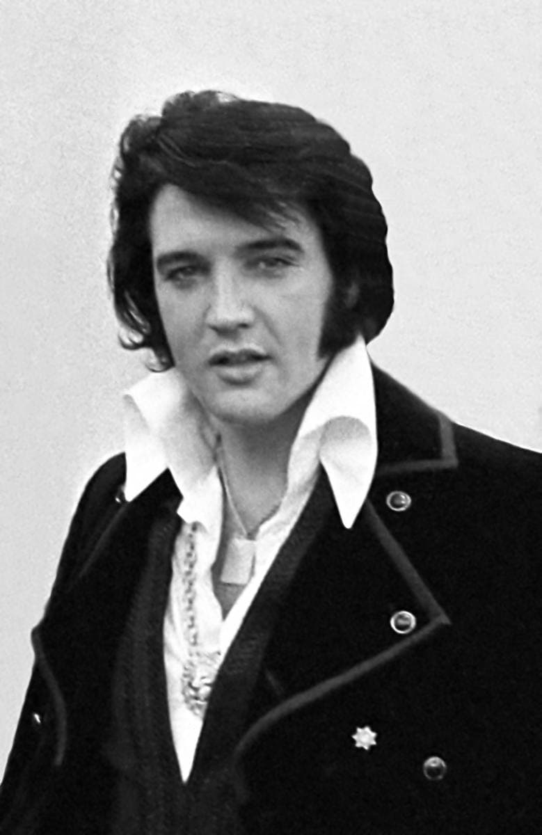 Elvis in a high-collared dark jacket and open white shirt