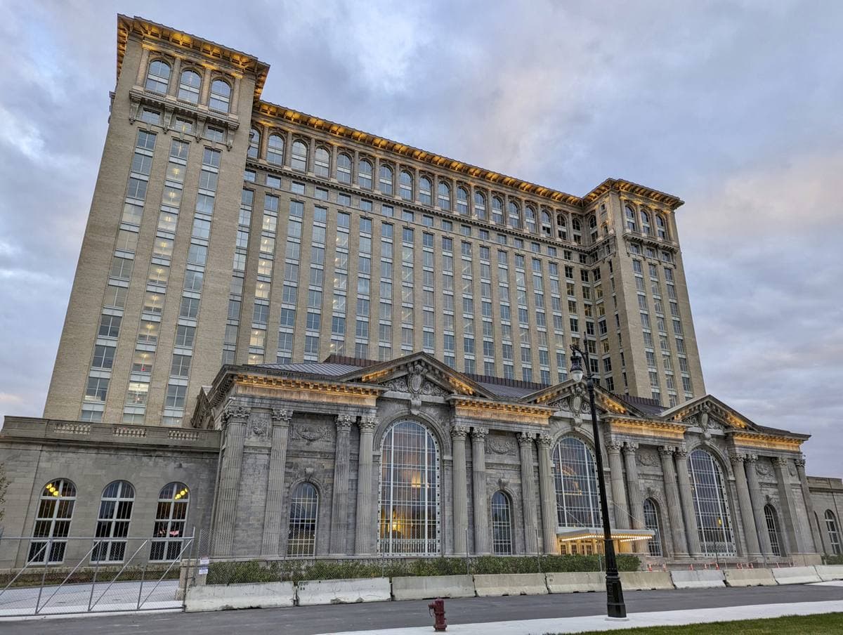 A tall Beaux-Arts station with a columned front and an office tower behind it under a blue sky