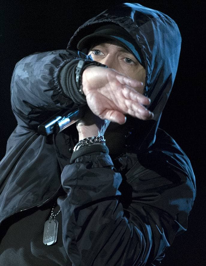 Eminem in a dark cap and hooded top performing with a microphone