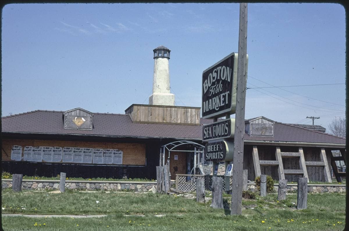 A low roadside fish market with a tall sign and a lighthouse-shaped tower beside 8 Mile Road under a pale sky