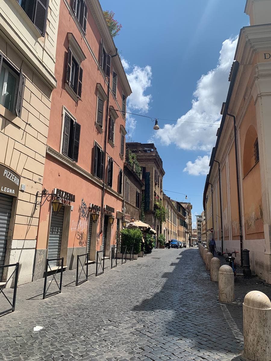 A narrow cobbled Trastevere street with ochre and pink houses under a blue sky