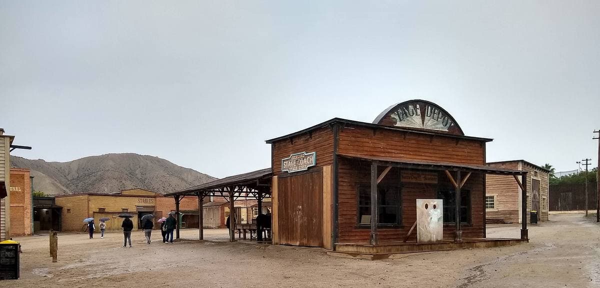 A dusty western street of timber fronts with a saloon sign, desert hills behind