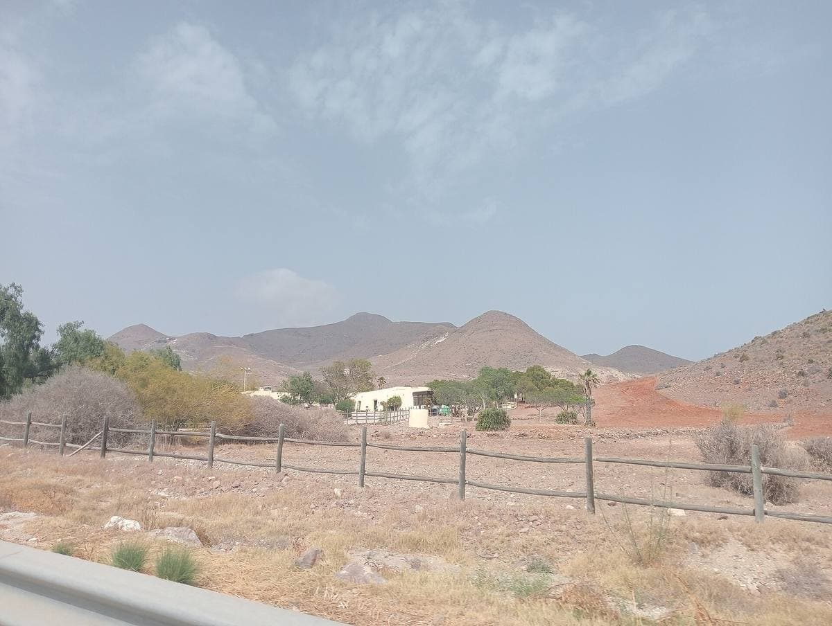 Dry fields and a low white farmhouse below bare hills
