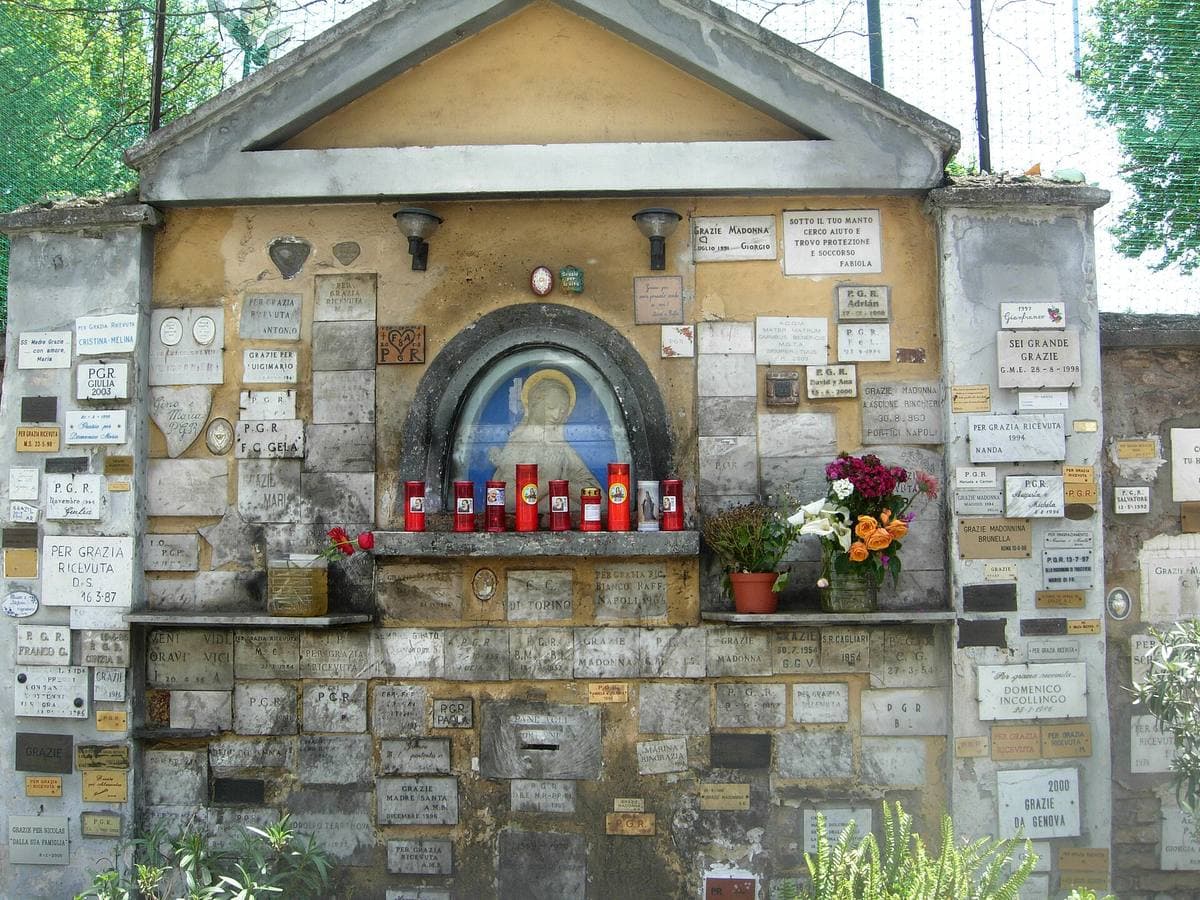 A painted street shrine with candles and flowers set into an old ochre wall on Viale Trastevere