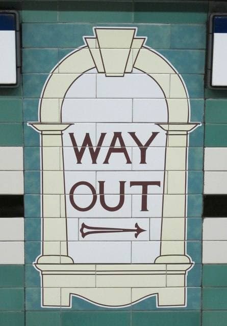 A tiled Way Out sign in a cream arch on a green London Underground wall