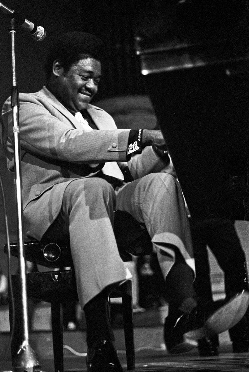 Fats Domino in a pale suit at a grand piano, one foot kicked up