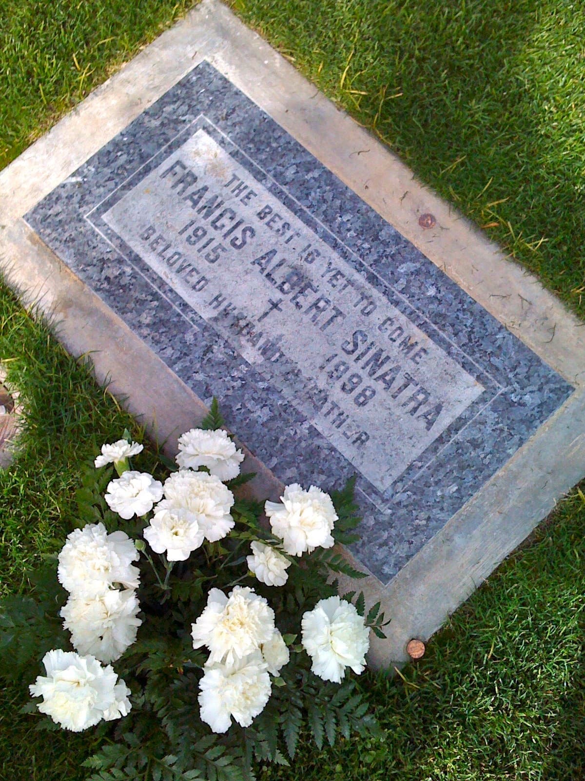 A flat grave marker in grass with small tributes on it