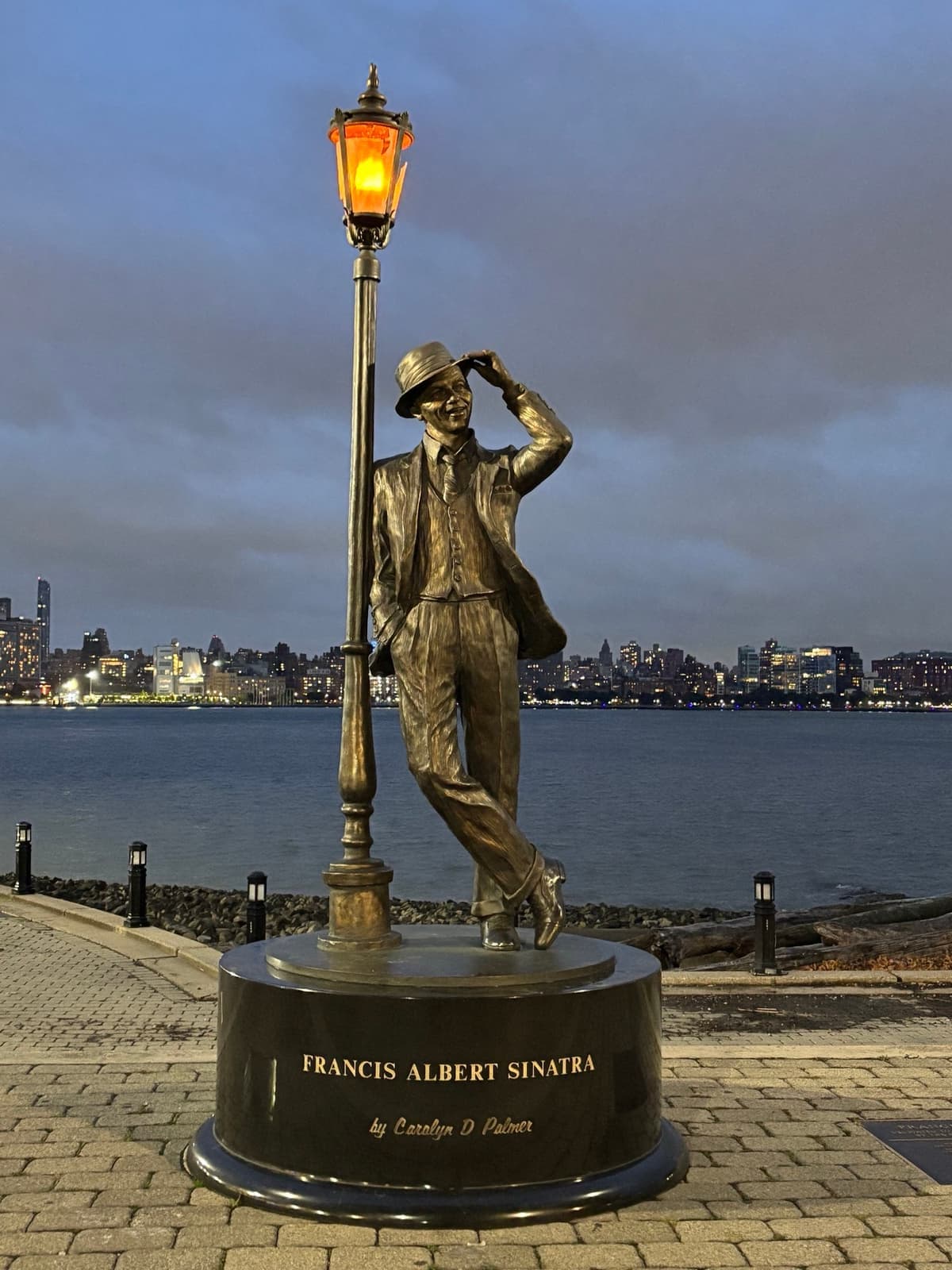 A bronze statue of Sinatra in a suit and hat leaning on a lamp post