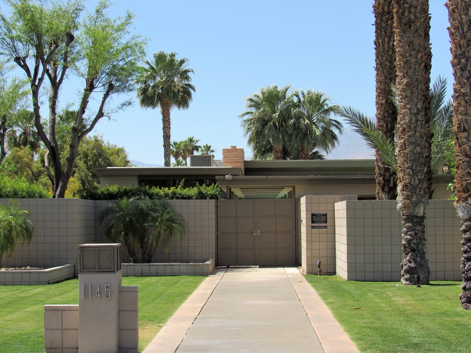 A low desert house behind a wall and palm trees