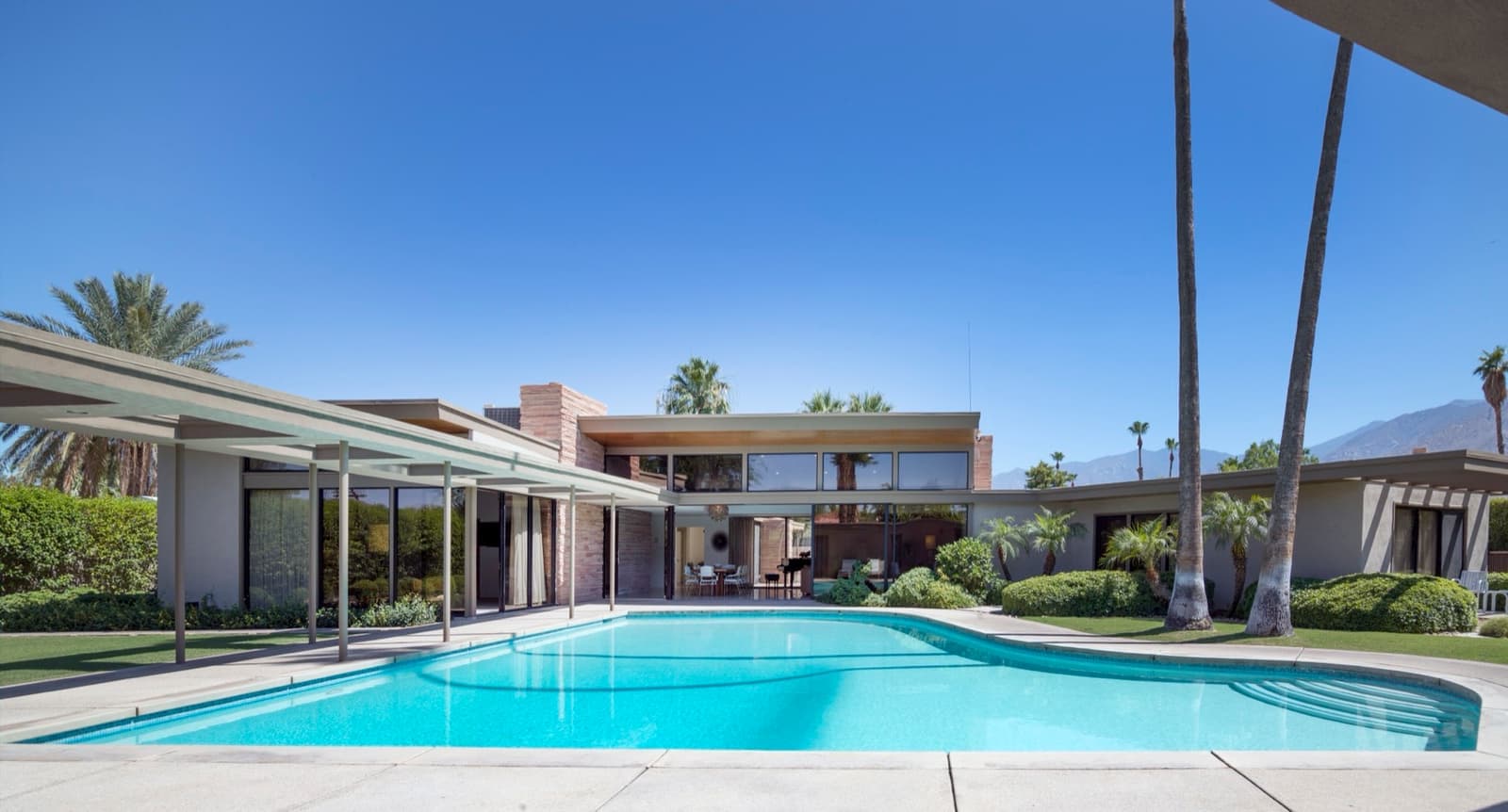 A low modernist house beside a pool under tall palms