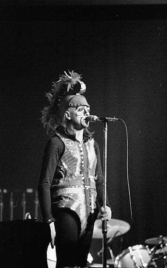 A singer in a Union Jack tunic, a plumed helmet and painted face, at a microphone