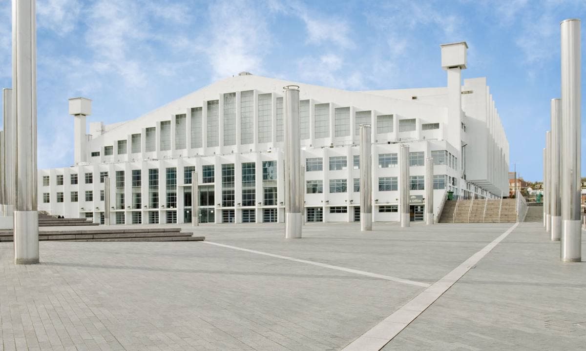 The long white front of Wembley Arena across an empty paved square under a blue sky
