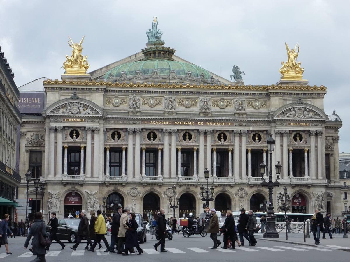 The gilded and columned front of the Palais Garnier with pedestrians crossing below