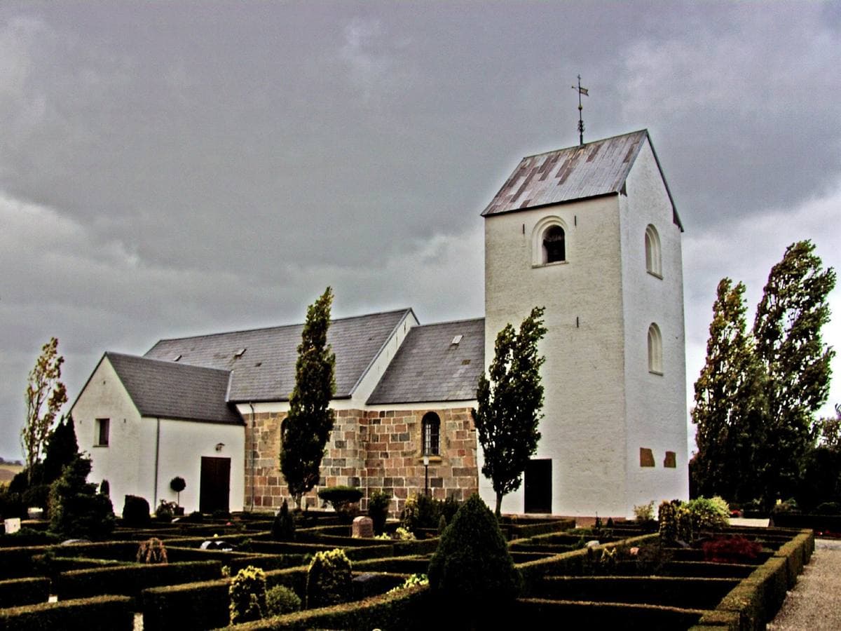 A whitewashed Danish village church with a tall square tower behind clipped hedges