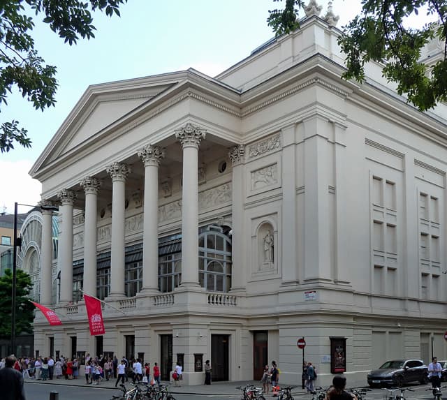 The white columned portico of the Royal Opera House on Bow Street with people on the pavement