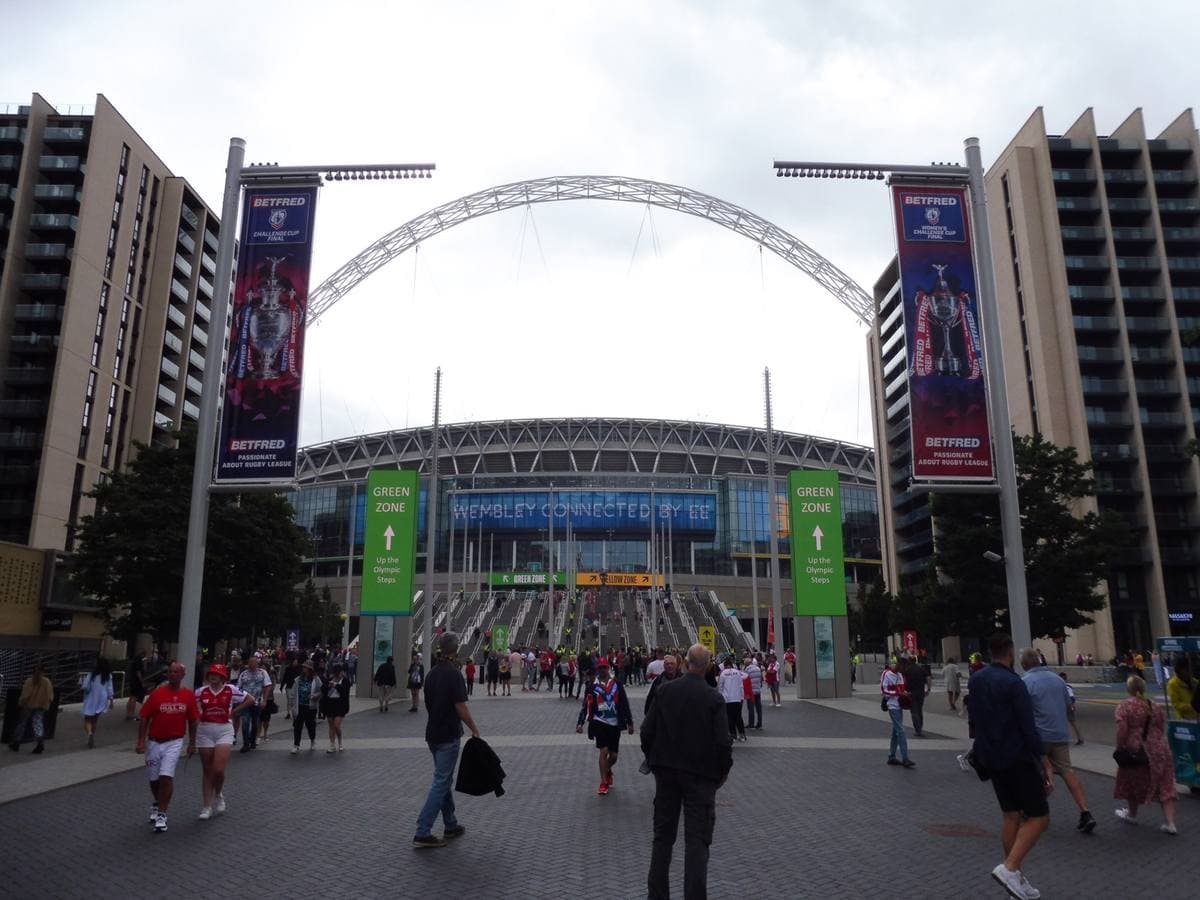 Crowds walking up Olympic Way towards Wembley Stadium under its white arch