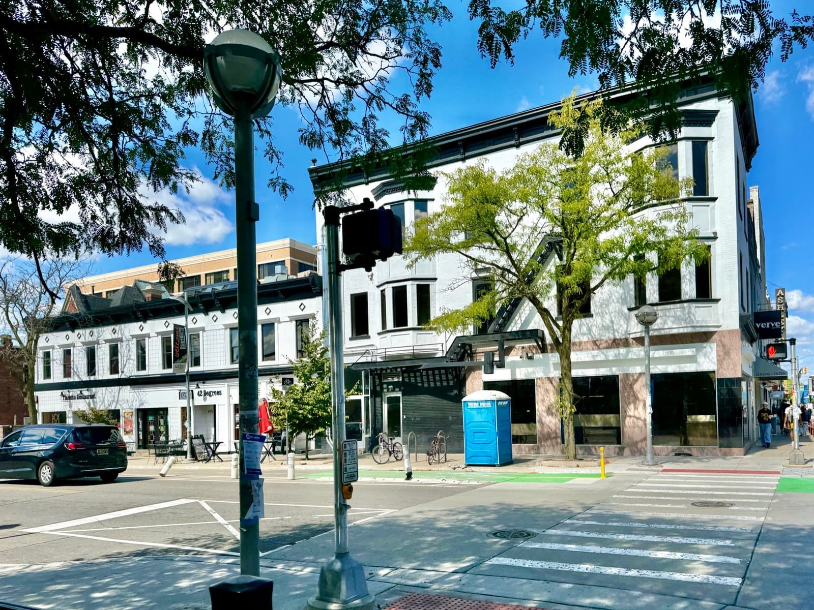 A sunny downtown Ann Arbor corner of old brick shopfronts with a crossing and a lamp post
