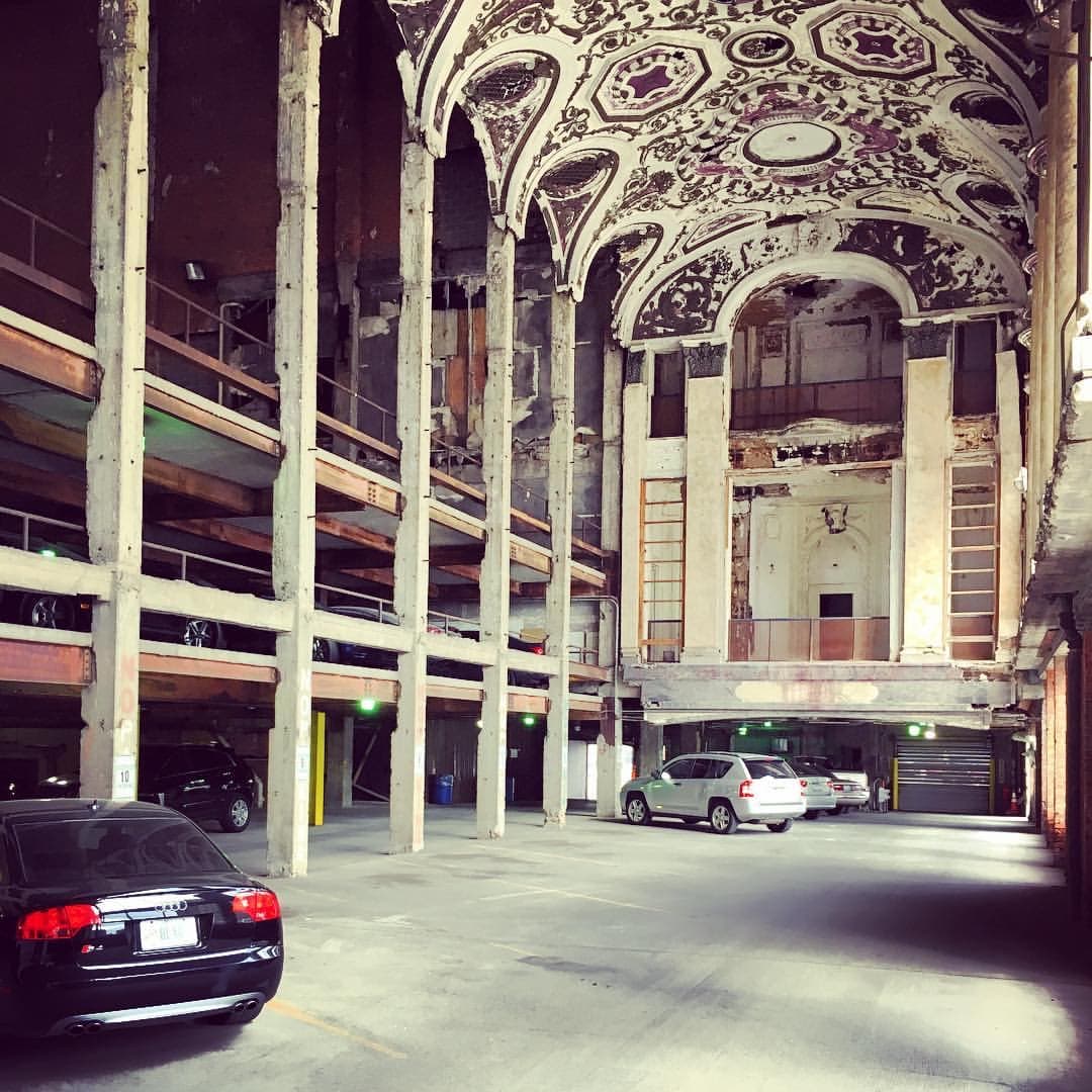 Concrete parking decks and columns rising inside a ruined, carved theatre auditorium